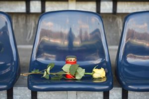 A yellow rose lies on a blue stadium seat and a red grave light stands on the seat.