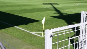 Eine Eckfahne, umgeben von einem Schatten eines Flutlichts und eines Tribünendachs.