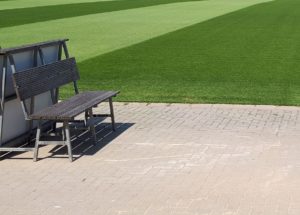 Eine Sitzbank steht am Spielfeldrand. Sie zeigt nicht auf das Spielfeld, sondern steht quer dazu.