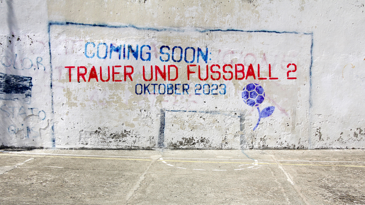 Auf einer Betonwand ist ein Tor aufgezeichnet, darin steht "Coming soon. Trauer und Fußball 2, Oktober 2023". Daneben ist unser Logo "Blume mit Fußballblüte" in lilal abgebildet.