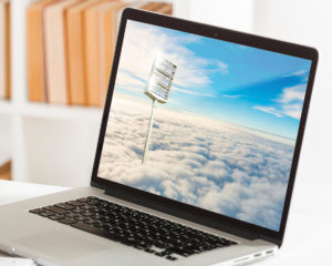 Ein aufgeklappter Laptop, der auf einem Tisch steht, zeigt ein Flutlicht, das auf den Wolken steht und in den blauem Himmel ragt.